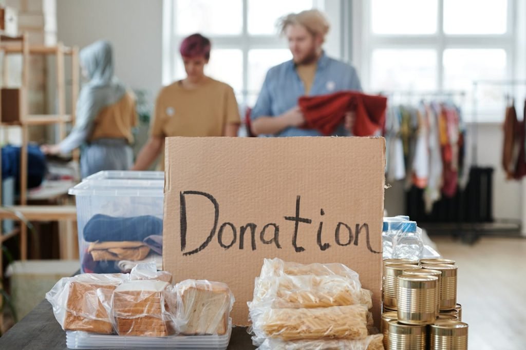 Volunteers sort clothes and food in a donation center. Cardboard sign reads Donation.